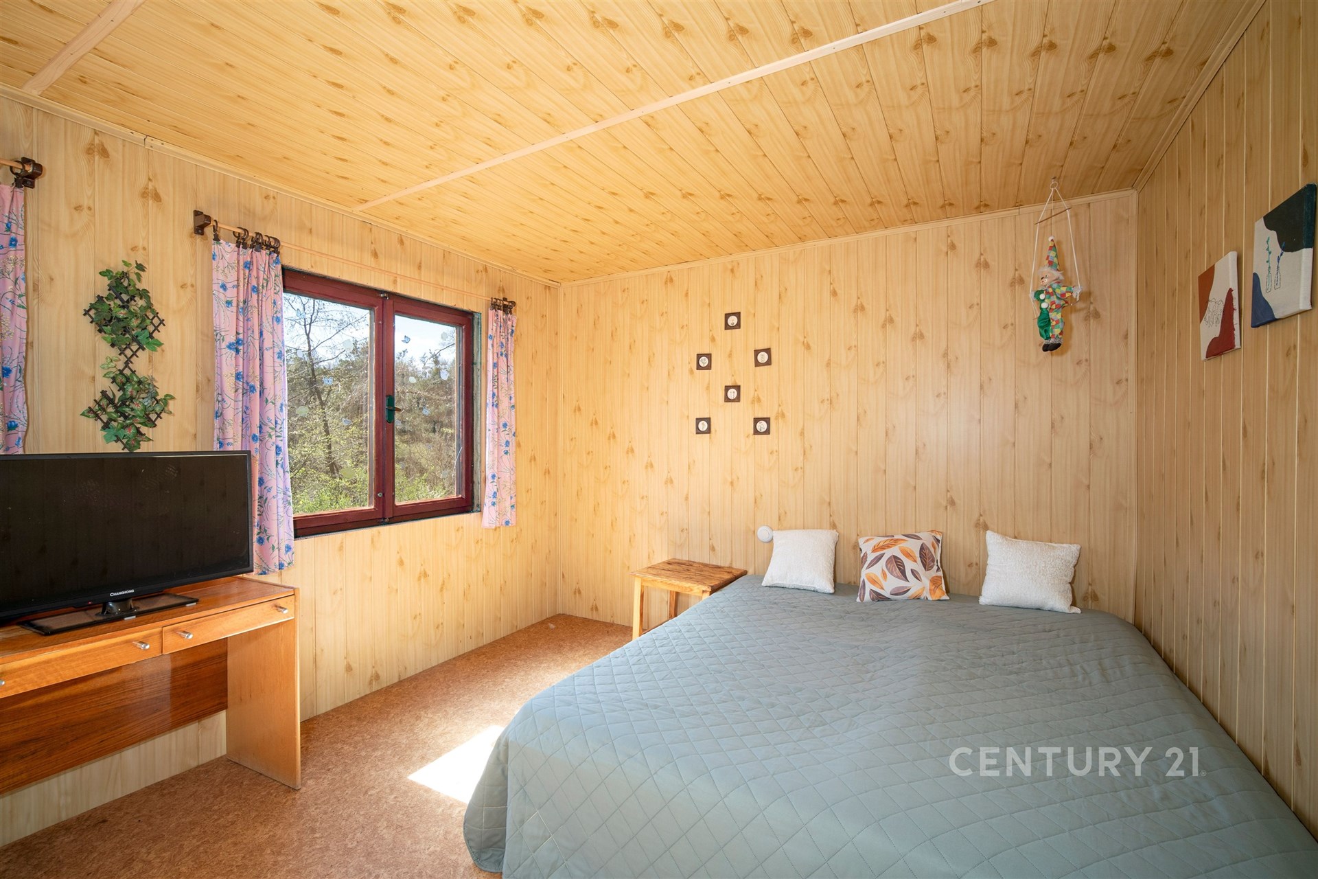 Ložnice s dřevěným obkladem, velkým oknem a manželskou postelí, nabízí útulný a přírodní styl.