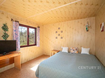 Ložnice s dřevěným obkladem, velkým oknem a manželskou postelí, nabízí útulný a přírodní styl. | Prodej - pozemek, zahrada, 380 m²