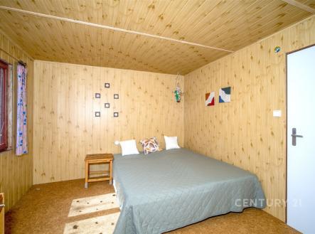 Ložnice s dřevěným obložením, velkými okny a parketovou podlahou nabízí útulný a rustikální styl. | Prodej - pozemek, zahrada, 380 m²