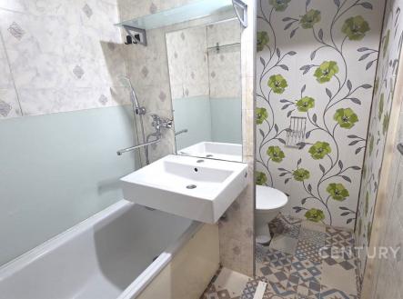 Rekonstruovaná koupelna s moderními obklady, vzorovanou dlažbou a velkým zrcadlem poskytuje stylový prostor pro relaxaci. | Pronájem bytu, 1+1, 33 m²