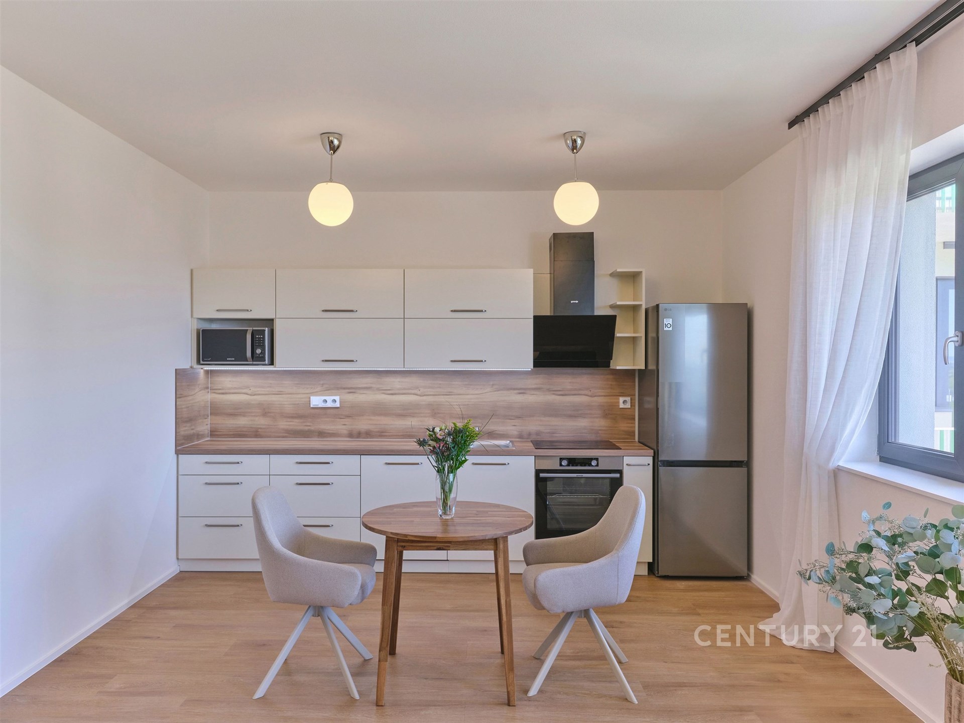 Moderní kuchyň s dřevěnou podlahou, světlým nábytkem a velkými okny, elegantní povrchová úprava, prostorný design, vynikající světelnost.