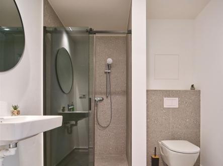 Moderní koupelna s dlažbou, prosklený sprchový kout a minimalistický design, elegantní umyvadlo a závěsné WC pro svěží vzhled. | Prodej bytu, 1+kk, 39 m²