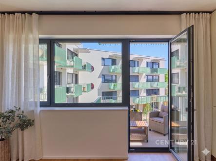 Světlý obývací pokoj s velkými okny, parketovou podlahou a moderním balkonem nabízí výhled na sousední budovy. | Prodej bytu, 1+kk, 39 m²