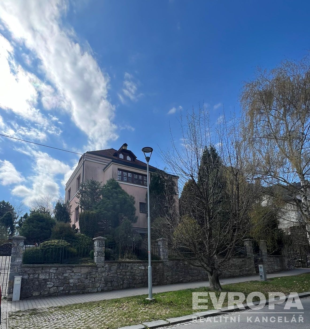 Vila s kamenným plotem, zasazená v udržované zahradě, nabízí klidné prostředí. Tradiční styl s moderními prvky, ideální pro prostorné bydlení.