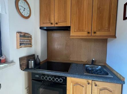 Malá kuchyň s dřevěnými skříněmi, elektrickým sporákem a dlažbou. Má praktické uspořádání a je ideální pro menší prostory. | Pronájem bytu, garsoniéra, 30 m²