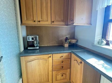 Kuchyň s dřevěnými skříňkami, moderními spotřebiči a dlažbou. Velká okna poskytují světlost a pohled na okolní krajinu. | Pronájem bytu, garsoniéra, 30 m²