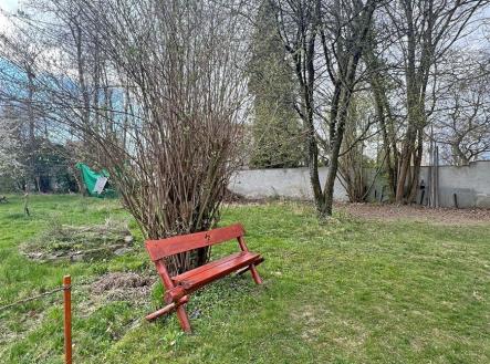 Zahrada s travnatým povrchem, vzrostlými stromy a dřevěnou lavičkou, ideální pro relaxaci, klidná lokalita. | Prodej - pozemek, zahrada, 1 441 m²