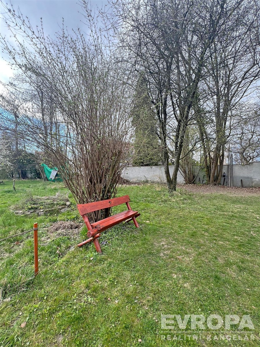 Zahrada s travnatým povrchem, vzrostlými stromy a dřevěnou lavičkou, ideální pro relaxaci, klidná lokalita.