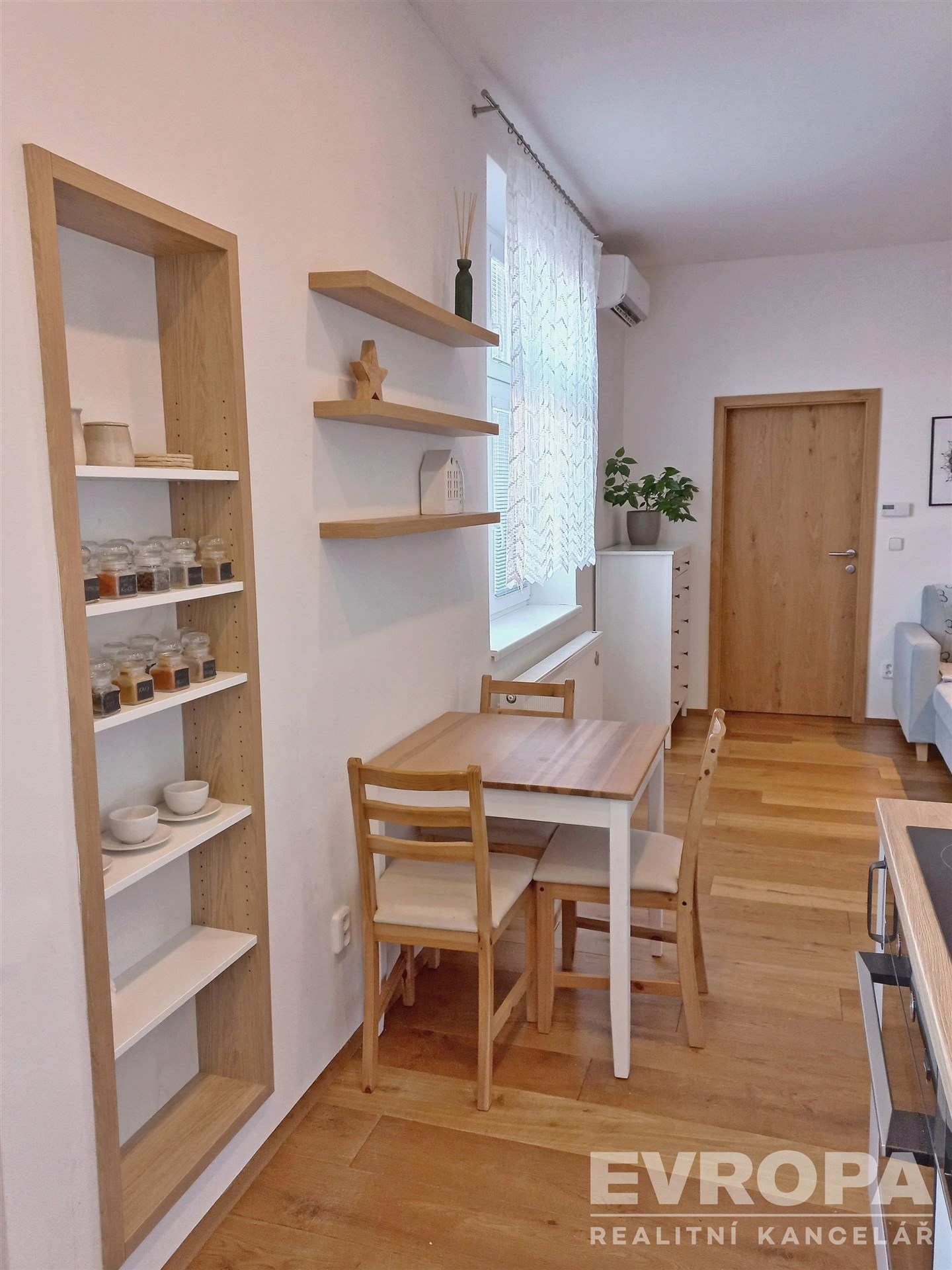 Jídelní kout s parketovou podlahou, světlý interiér, dřevěný stůl a police, moderní nábytek, útulné bydlení v moderním stylu.