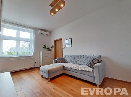 Světlý obývací pokoj s parketovou podlahou, velkými okny a moderním osvětlením, nabízí pohodlný prostor s klimatizací a minimalistickým designem. | Pronájem bytu, 2+kk, 54 m²