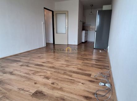 Prázdný obývací pokoj s parketovou podlahou, světlý interiér s moderním stylem, v pozadí kuchyňská linka. | Prodej bytu, 2+kk, 45 m²