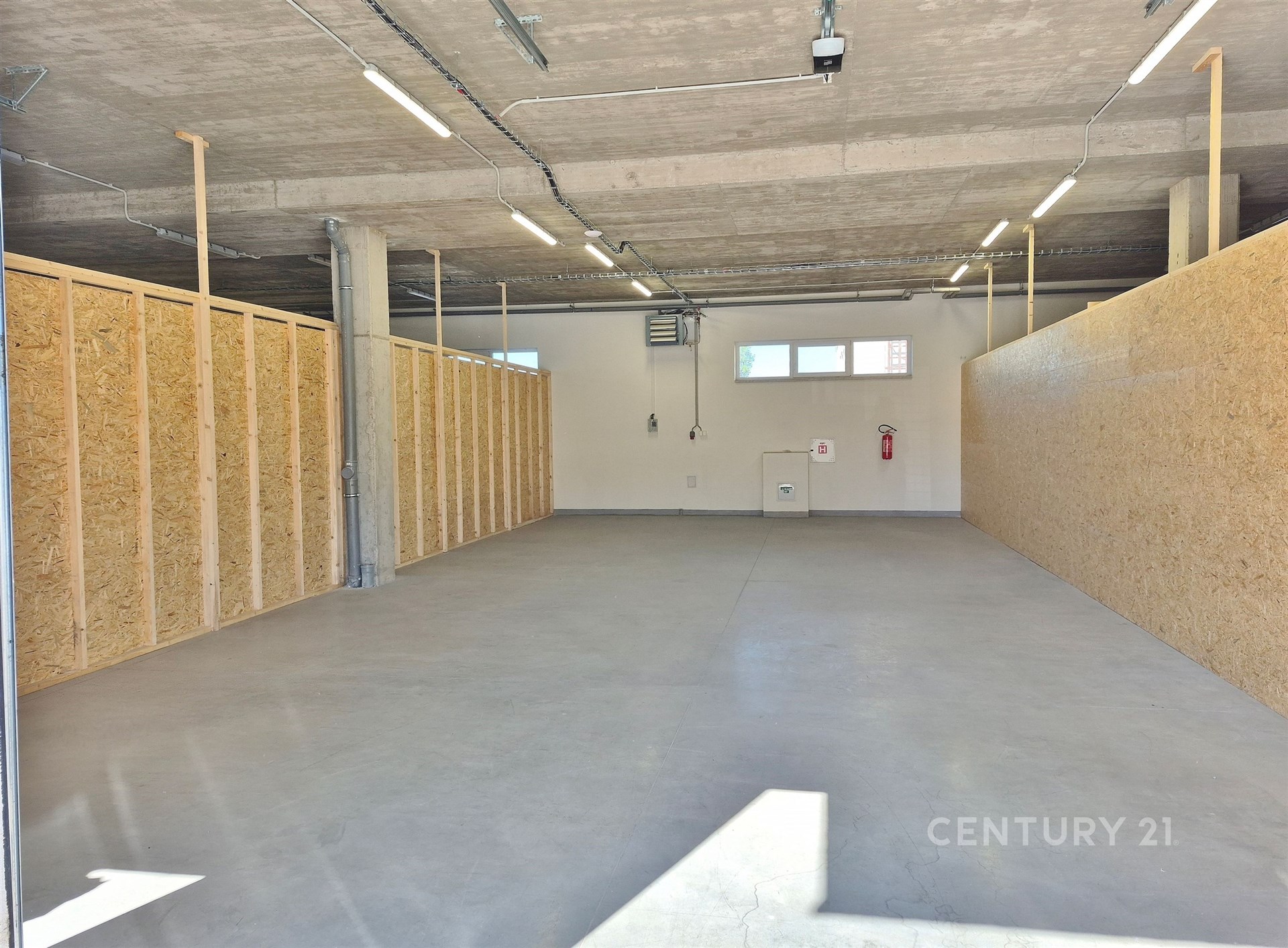 Prostorná garáž s betonovou podlahou a dřevěnými příčkami, světlý průmyslový styl, ideální pro skladování nebo parkování.