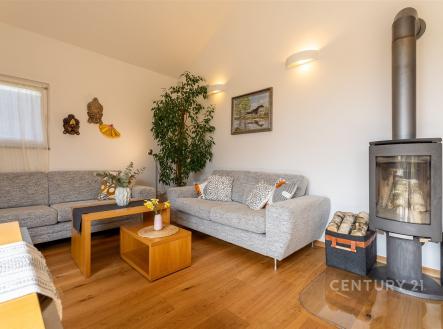 Světlý obývací pokoj s krbovými kamny, dřevěnou podlahou a moderním nábytkem nabízí útulné a stylové prostředí. | Prodej - dům/vila, 115 m²