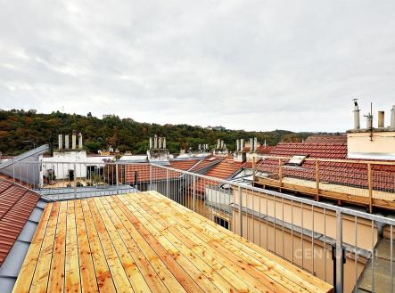 Střešní terasa s dřevěnou podlahou, nabízející výhled na okolní střechy a zeleň, vhodná pro relaxaci a venkovní posezení. | Pronájem bytu, 3+kk, 134 m²