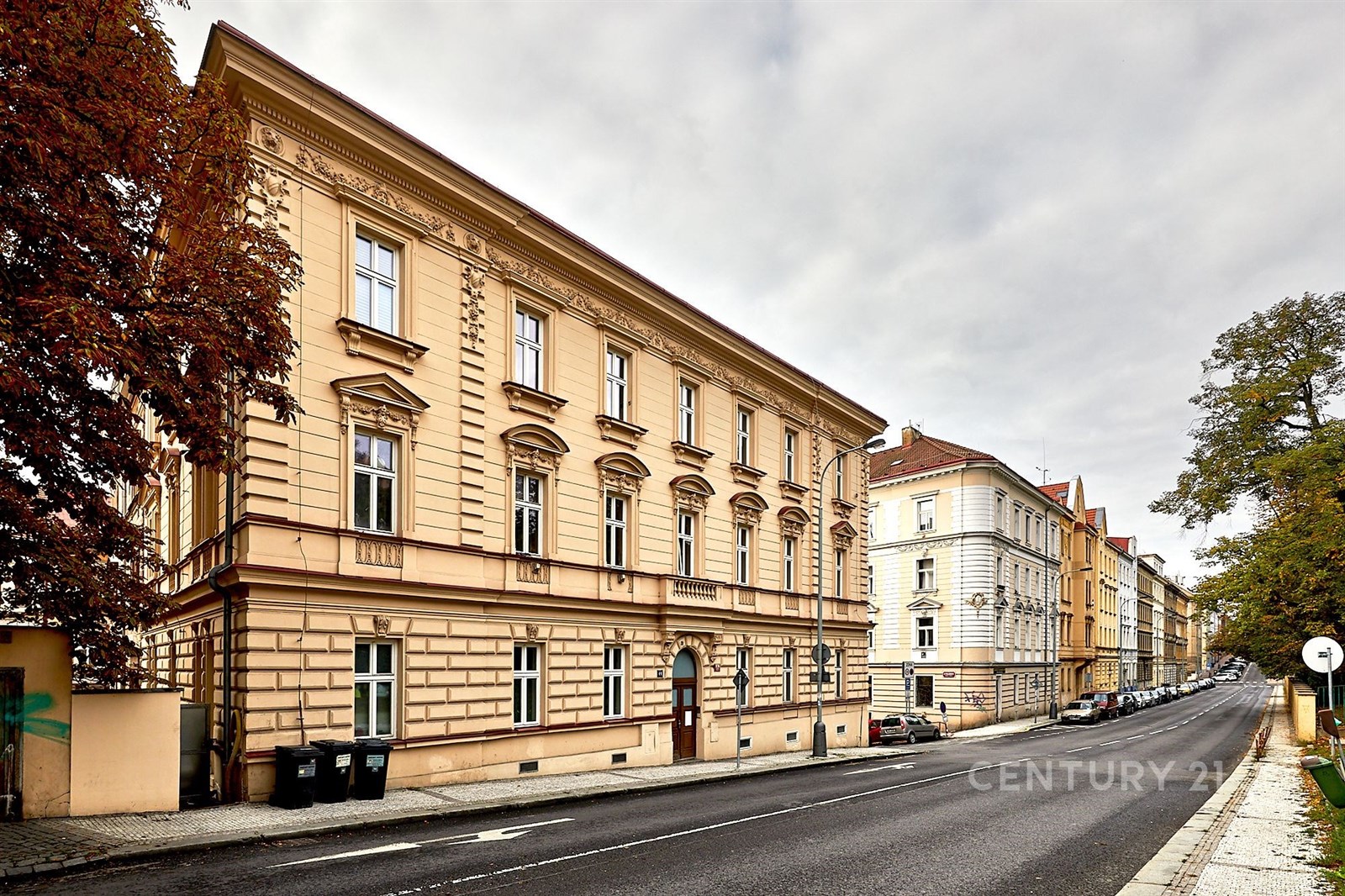 Historická fasáda bytového domu s tradičními architektonickými prvky na klidné ulici, renovovaný exteriér s okny do ulice, udržované okolí.