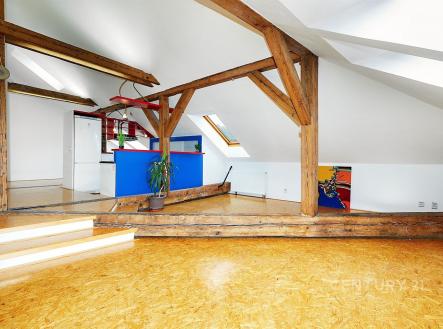Podkrovní prostor s dřevěnými trámy, parketovou podlahou a moderními prvky, nabízí světlý interiér s vestavěnými doplňky a uměleckým akcentem. | Pronájem bytu, 3+kk, 134 m²
