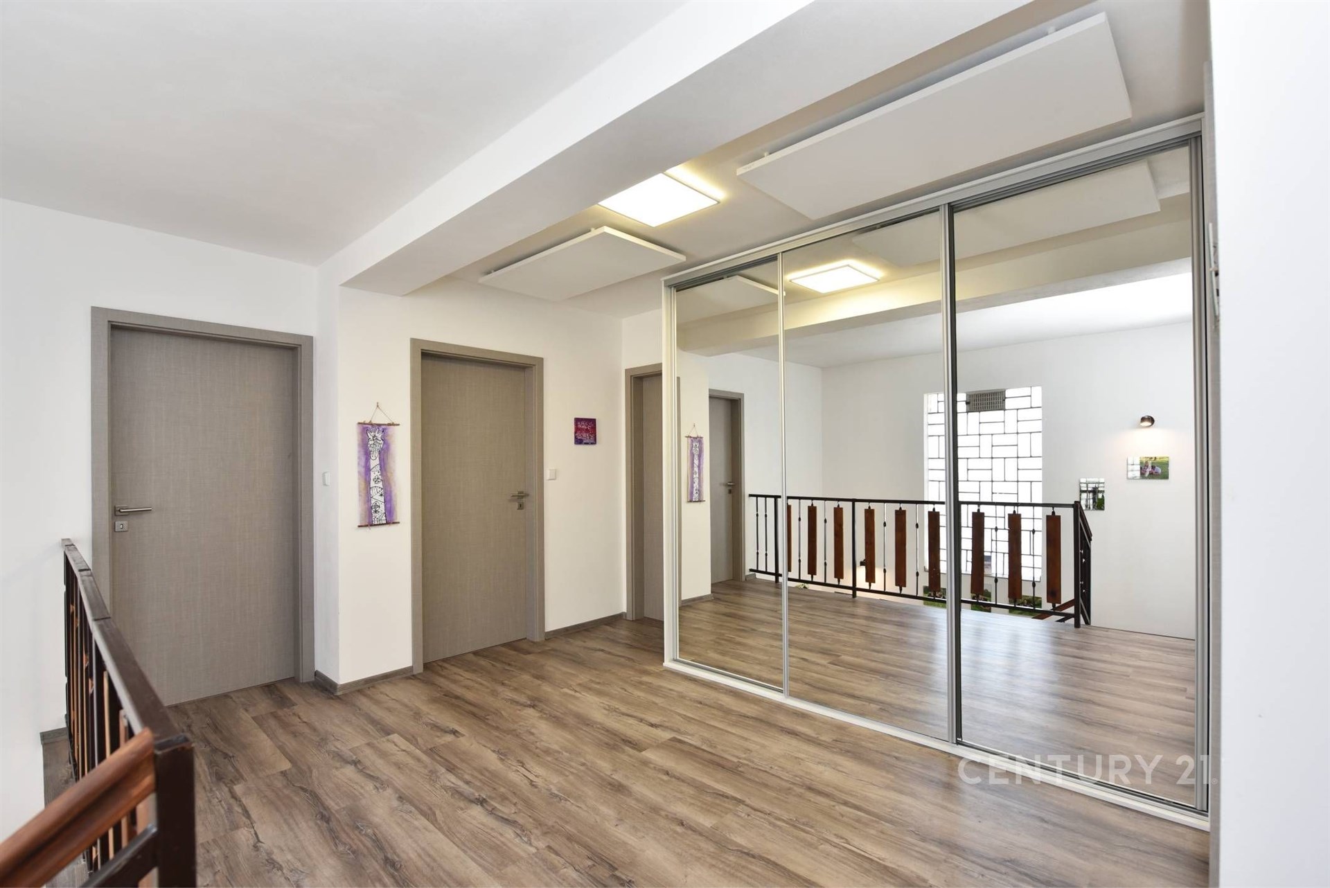 Chodba s laminátovou podlahou, vestavěné skříně a moderní design, světlý prostor díky velkým oknům a minimalistické osvětlení.