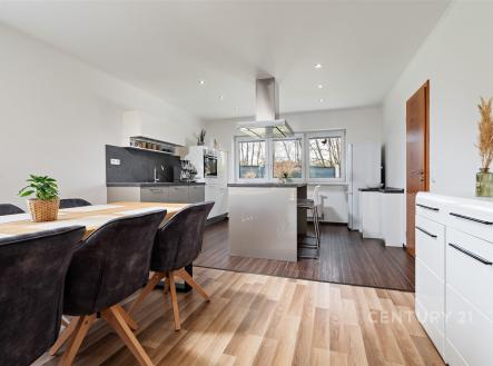 Moderní kuchyň s parketovou podlahou, velkými okny a vestavěnými spotřebiči. Světlý otevřený prostor s dřevěným jídelním stolem a světlým interiérem. | Prodej - dům/vila, 146 m²