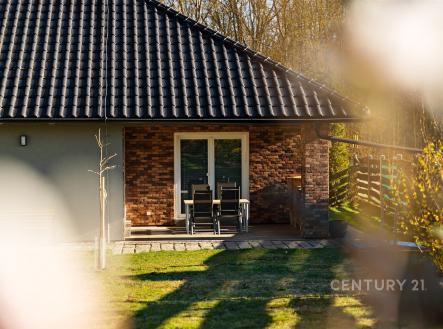 Exteriér domu s terasou, cihlovým obkladem a velkými okny, moderní styl. Udržovaná zahrada dodává příjemnou atmosféru. | Prodej - dům/vila, 146 m²