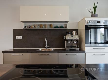 Moderní kuchyň s vestavěnými spotřebiči, tmavou pracovní deskou a lakovanými skříňkami, stylový design a kvalitní materiály. | Prodej - dům/vila, 146 m²