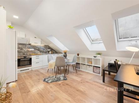 Podkrovní kuchyň a jídelna s moderními spotřebiči, dřevěnou podlahou a velkými střešními okny, vytvářející světlý prostor. | Prodej bytu, 3+kk, 45 m²
