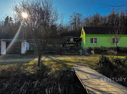 Zahrada s dřevěným chodníkem před zeleným rodinným domem, dvě garáže, klidná lokalita, ideální pro rodiny hledající venkovské bydlení. | Prodej - dům/vila, 93 m²