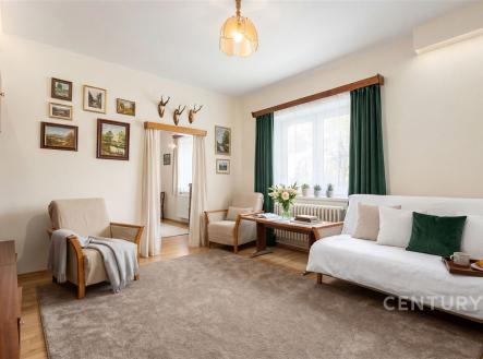 Světlý obývací pokoj s parketovou podlahou, velkými okny a pohodlným posezením, dekorativní obrazy na stěnách, stylově zařízený interiér. | Prodej - dům/vila, 93 m²