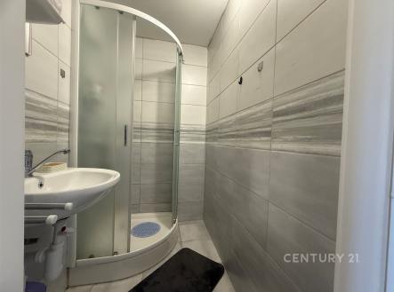 Moderní koupelna s dlažbou, sprchovým koutem a umyvadlem. Světlé keramické obklady dodávají prostoru elegantní vzhled. | Prodej bytu, 1+kk, 31 m²
