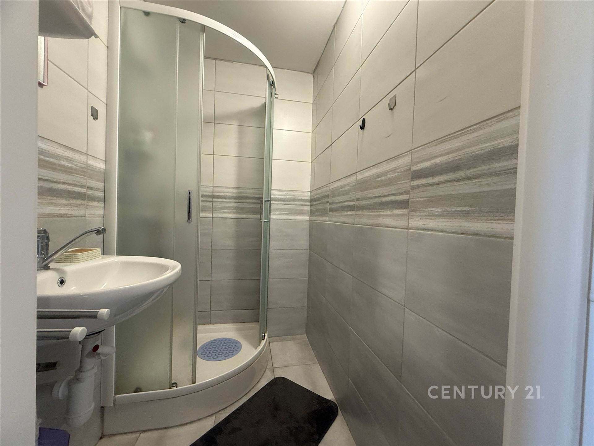 Moderní koupelna s dlažbou, sprchovým koutem a umyvadlem. Světlé keramické obklady dodávají prostoru elegantní vzhled.