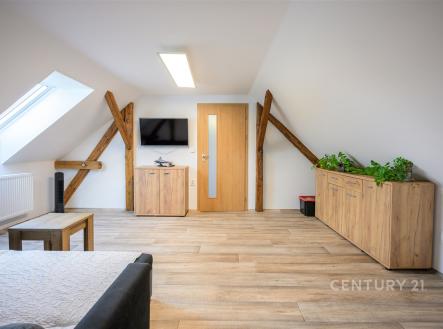 Podkrovní obývací pokoj s dřevěnou podlahou, masivním nábytkem a šikmým stropem poskytuje útulnou atmosféru a moderní styl bydlení. | Prodej - dům/vila, 180 m²
