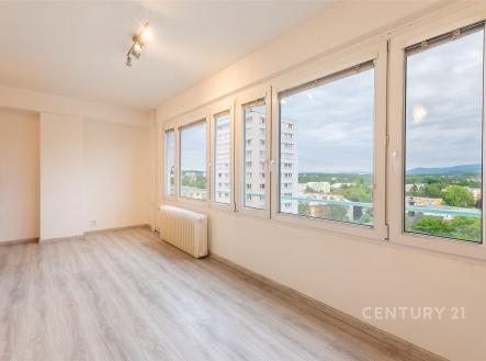 Světlý obývací pokoj s velkými okny, moderní laminátovou podlahou a výhledem na okolí, nabízí prostorný a útulný interiér. | Prodej bytu, 1+kk, 23 m²