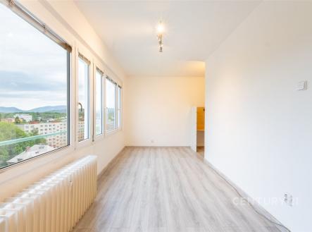 Světlý obývací pokoj s velkými okny, moderní parketová podlaha, výhled na město, minimalistické bílé stěny, prostorný vzhled. | Prodej bytu, 1+kk, 23 m²