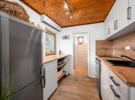 Kompaktní kuchyň s moderními spotřebiči, dřevěným obkladem a světlými skříňkami. Dřevěná podlaha dodává příjemnou atmosféru. | Prodej - dům/vila, 90 m²