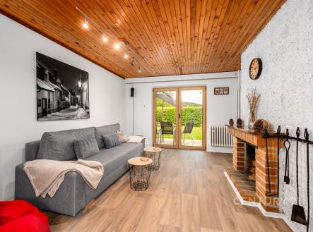 Světlý obývací pokoj s dřevěným stropem, krbovými kamny a velkými okny. Moderní parketová podlaha dodává prostoru elegantní vzhled. | Prodej - chata/rekreační objekt, 90 m²