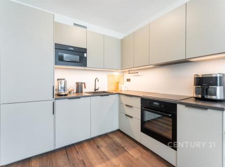 Moderní kuchyň s vestavěnými spotřebiči, parketová podlaha, světlé skříňky a dřevěné detaily, elegantní a funkční design. | Prodej bytu, 2+kk, 57 m²