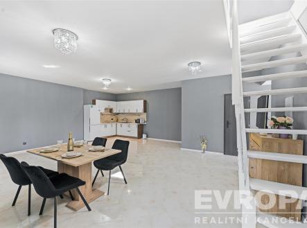 Prostorná jídelna s moderní dlažbou, dřevěným nábytkem a vestavěnou kuchyňskou linkou. Velká okna a elegantní osvětlení dodávají prostoru světlo. | Prodej - dům/vila, 114 m²