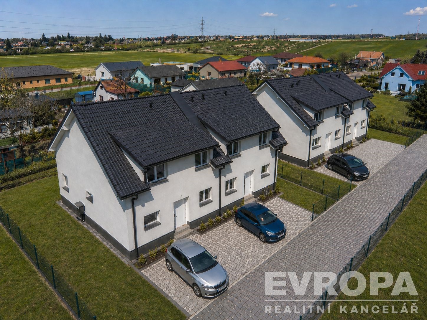 Řadové rodinné domy s moderní fasádou a parketovými příjezdovými cestami, obklopené zelení a nacházející se v klidné oblasti.