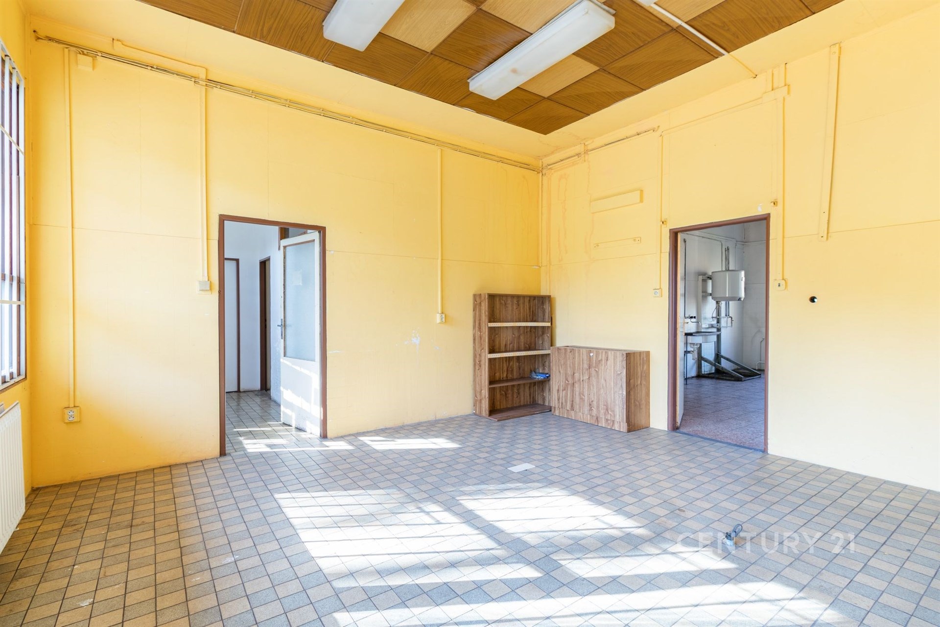 Světlý pokoj s dlažbou, velkými okny a vestavěnými skříněmi, ideální pro rekonstrukci nebo modernizaci v bytovém domě.