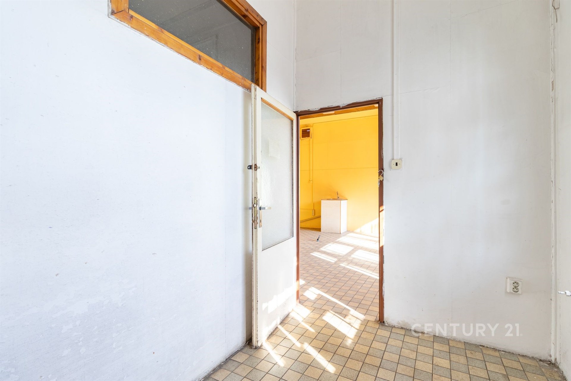 Vstupní hala s dlažbou, vysoké stropy a dveře vedou do světlé místnosti s velkými okny, ideální pro moderní rekonstrukci.