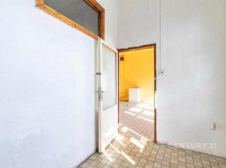 Vstupní hala s dlažbou, vysoké stropy a dveře vedou do světlé místnosti s velkými okny, ideální pro moderní rekonstrukci. | Pronájem - obchodní prostor, 64 m²