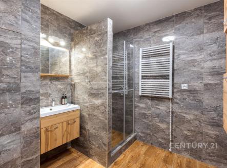 Moderní koupelna s dlažbou, sprchovým koutem a vestavěným umyvadlem. Dřevěná skříňka a světlé osvětlení dodávají elegantní vzhled. | Prodej bytu, 3+1, 67 m²
