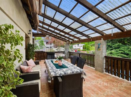 Krytá terasa s dlažbou, zahradním nábytkem a dřevěným zábradlím nabízí pohodlné venkovní posezení. | Prodej - dům/vila, 261 m²