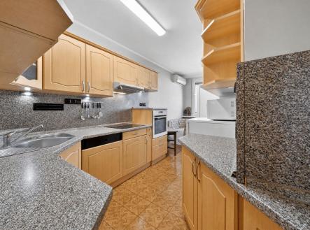 Moderní kuchyň s dřevěnými skříňkami, žulová pracovní deska, vestavěné spotřebiče a dlažba. | Prodej bytu, 3+1, 84 m²