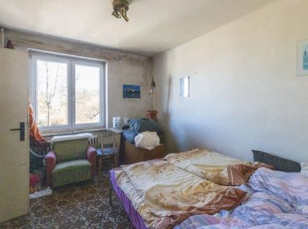 Světlá ložnice s velkým oknem, kobercem a staršími postelemi. Pokoj potřebuje rekonstrukci, nabízí potenciál pro modernizaci. | bytu, 3+1, 59 m²