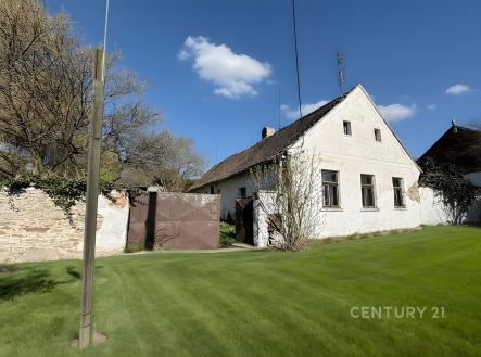 Tradiční venkovský dům s bílou fasádou, šikmou střechou a dřevěnými okny, obklopený zeleným trávníkem a kamenným plotem, ideální k rekonstrukci. | Prodej - chata/rekreační objekt, 156 m²