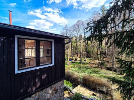 Výhled z dřevěné chaty s kamennou podezdívkou na udržovanou zahradu obklopenou stromy, přírodní materiály a malebná lokalita | Prodej - chata/rekreační objekt, 39 m²