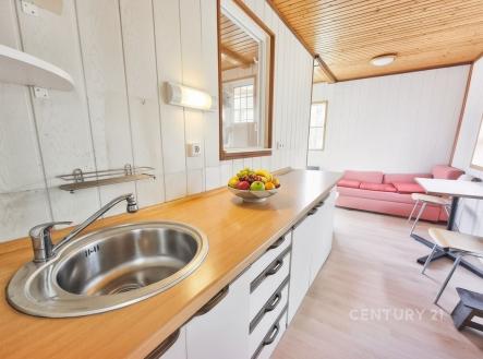 Kuchyň s dřevěnou pracovní deskou a vestavěným dřezem, přilehlým světlým obývacím pokojem s velkými okny a moderním designem | Prodej - chata/rekreační objekt, 39 m²