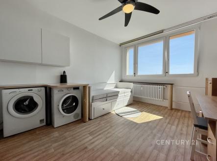 Světlý obývací pokoj s dřevěnou podlahou, velká okna, moderní interiér, v rohu místo pro praní s pračkou a sušičkou. | Pronájem bytu, 1+kk, 22 m²