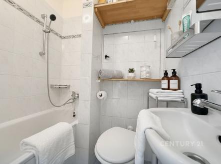 Malá koupelna s bílými dlaždicemi, moderními kovovými detaily a uspořádaným úložným prostorem. Světlý a funkční design. | Pronájem bytu, 1+kk, 22 m²