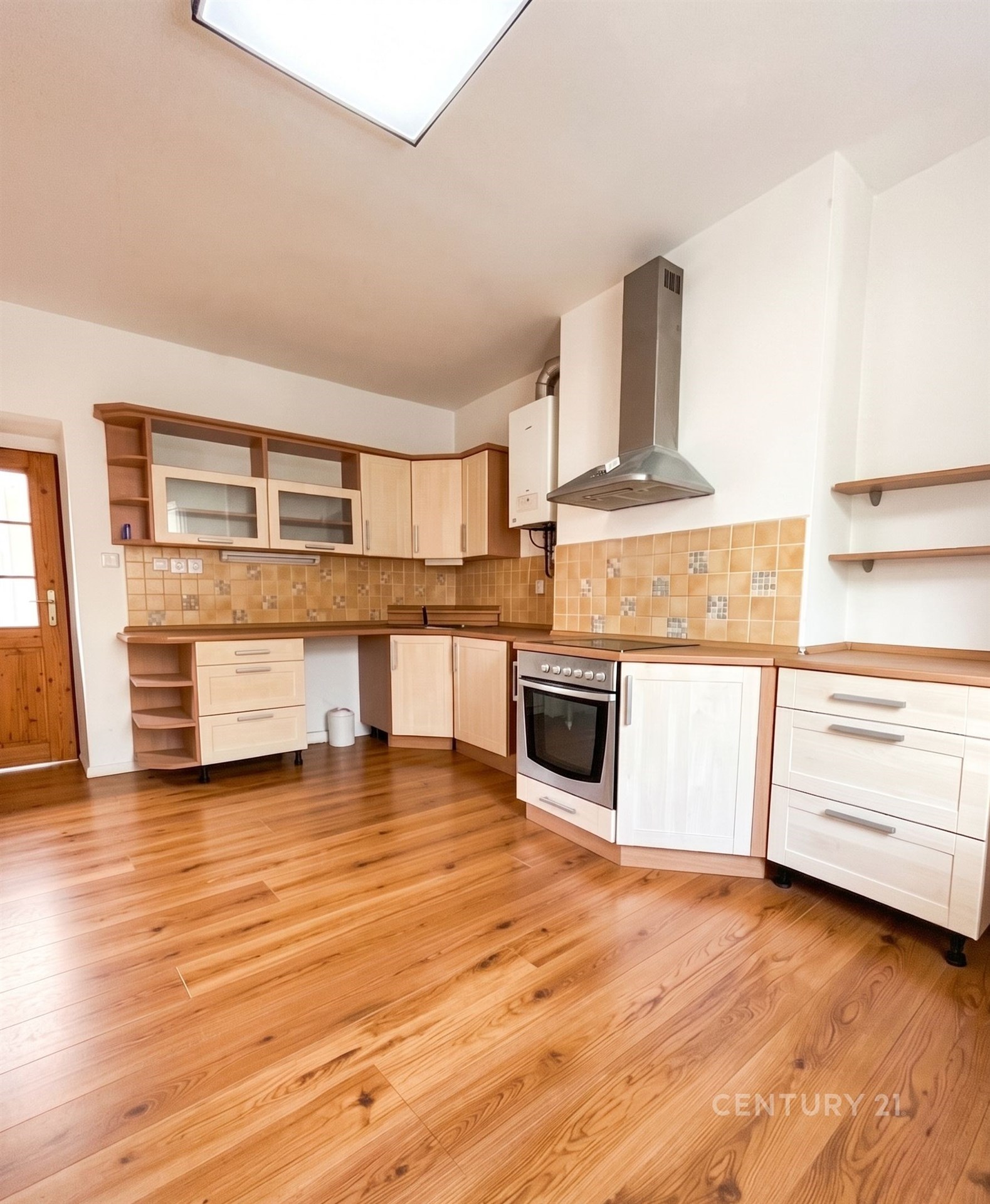 Kuchyň s parketovou podlahou a dřevěnými skříňkami, moderní spotřebiče a obklady stěn, světlý prostor s velkými okny.